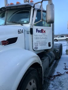 A white truck parked in the snow with fedex sign on it.